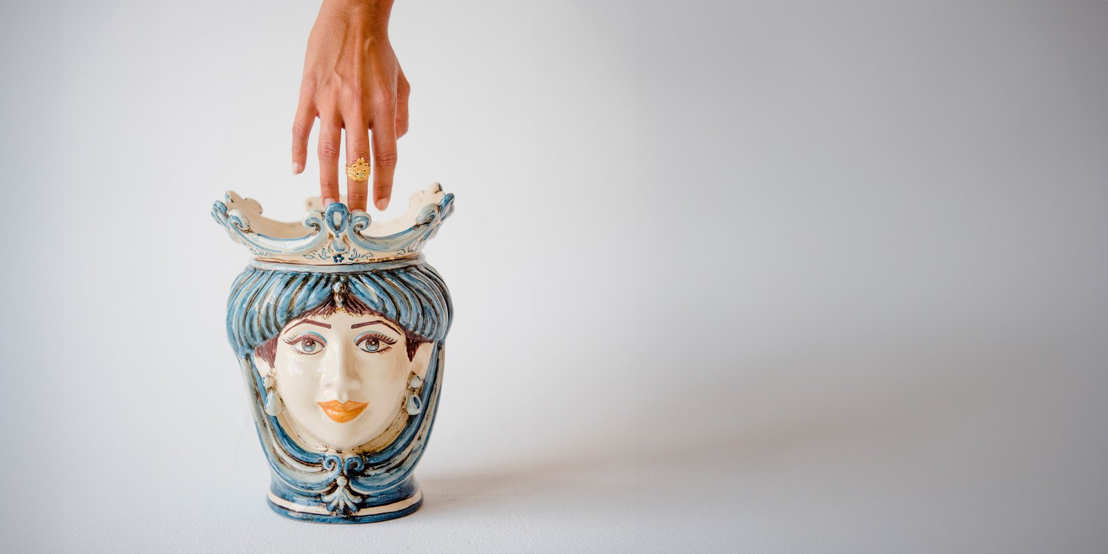 Blue and white Caltagirone piece from the Mono Blu line, with a hand resting on it for scale