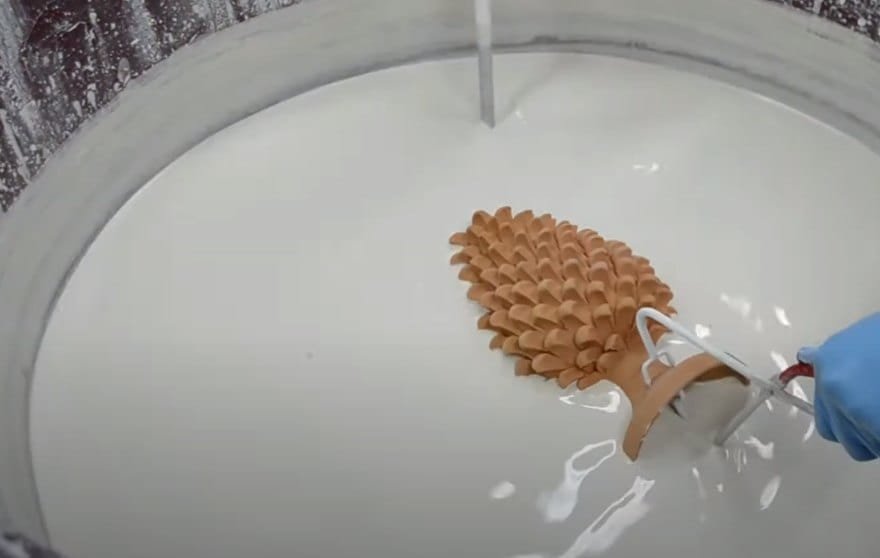 A ceramic pine cone dipped into a basin of white glaze